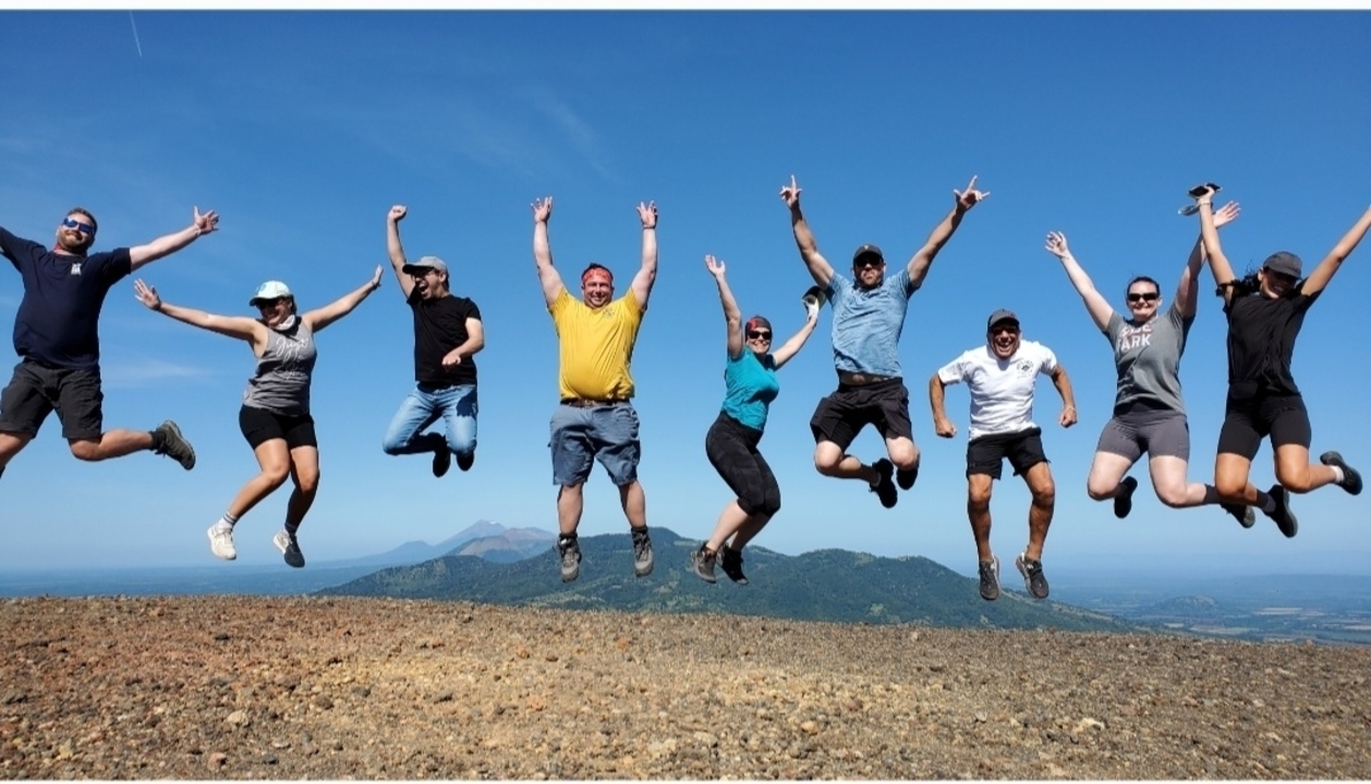 Group of people jumping in the air with mountains in the background.