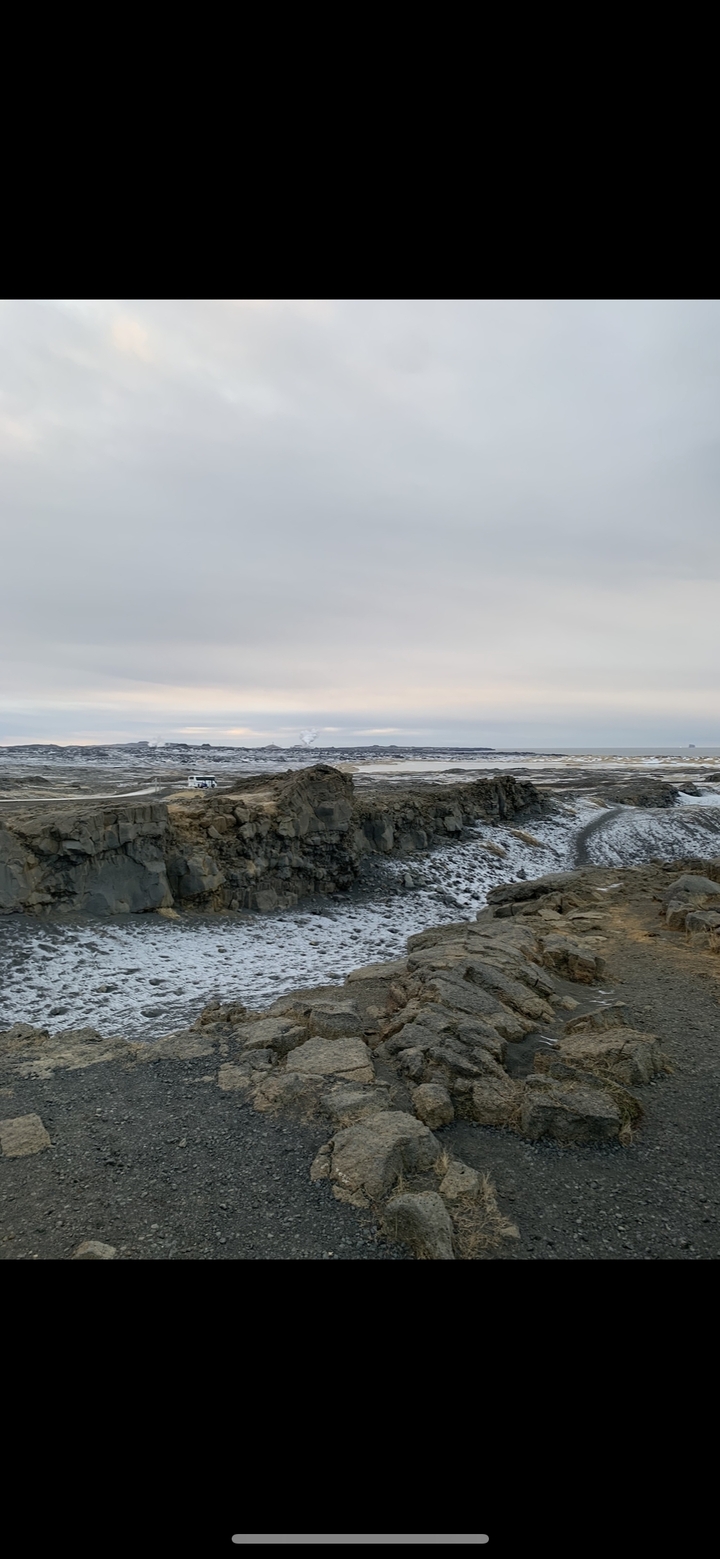 Cold, rocky landscape with a distant vehicle and steam.