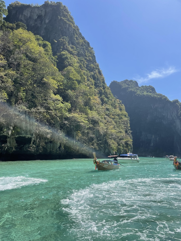 Traditional long boats on vibrant turquoise water surrounded by cliffs.