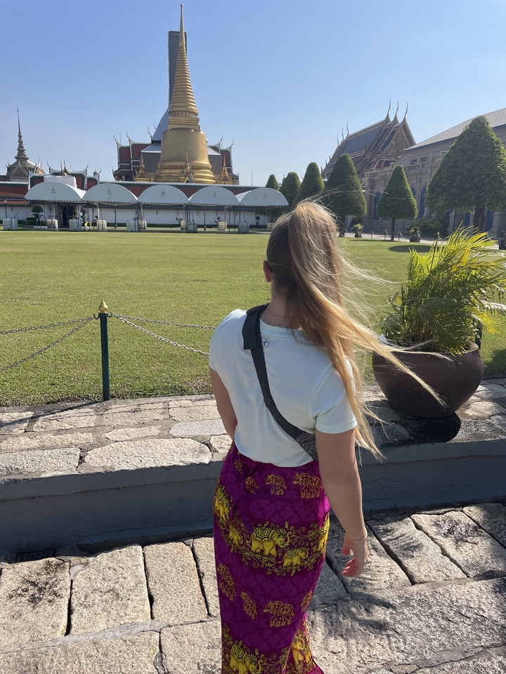 A person standing facing a large grassy area with trees and buildings.