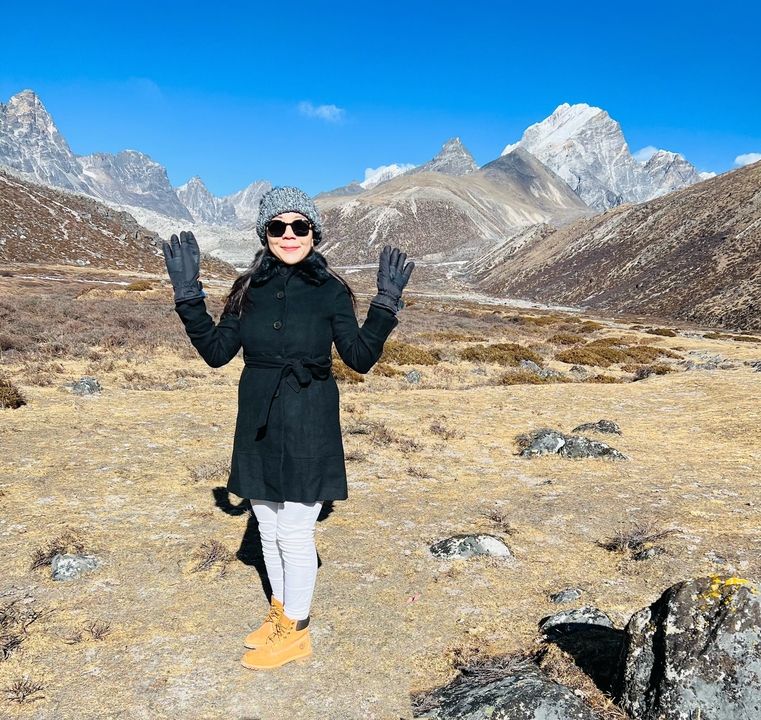 Woman with raised arms in a mountainous valley setting.