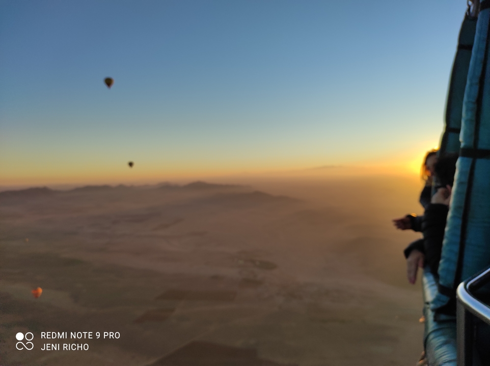 View from a hot air balloon during dawn with faint outlines of other balloons.