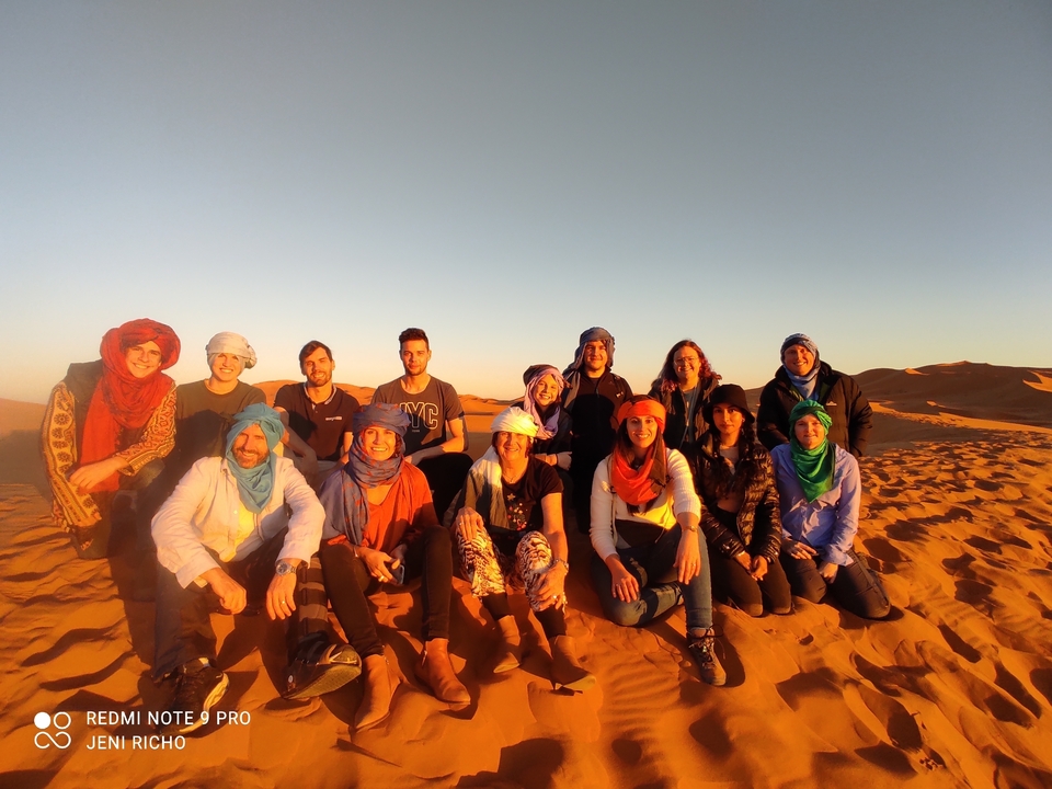 A group of people sitting on a sand dune at sunset.