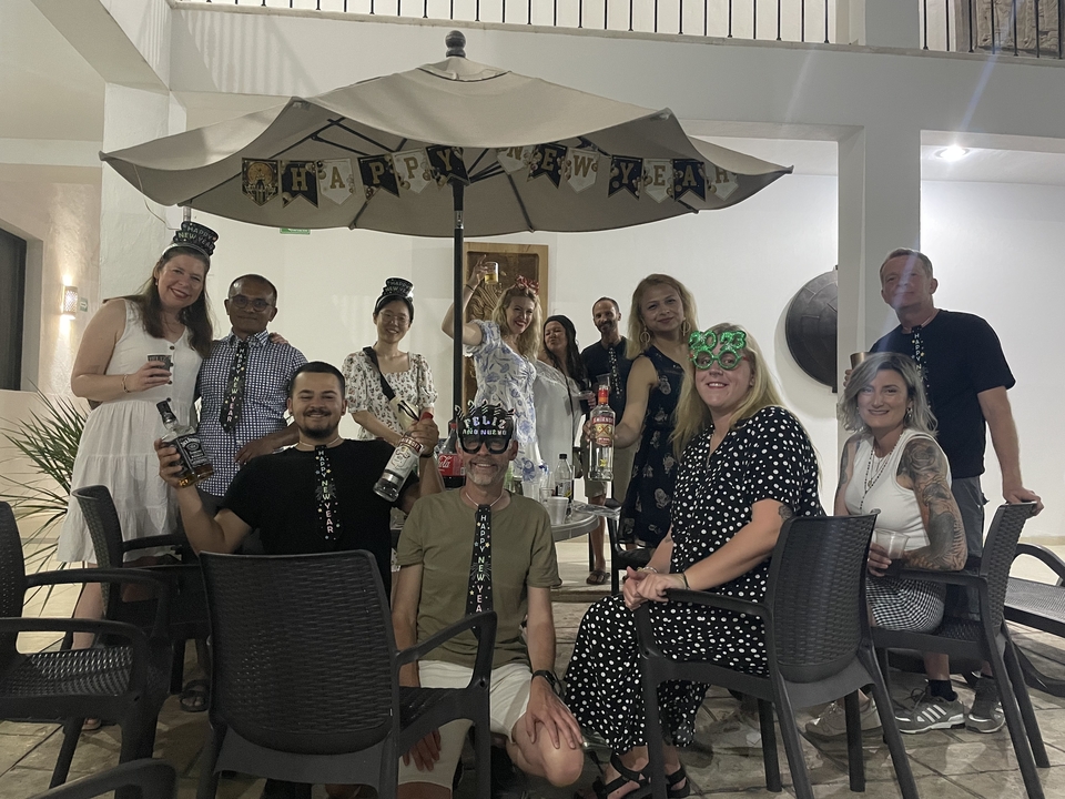 Une photo de groupe de personnes qui célèbrent avec des chapeaux de fête et des boissons sous une banderole « Bonne Année ».