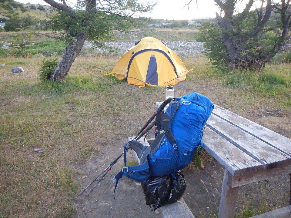 Camping scene with a yellow tent and backpack next to a picnic table.