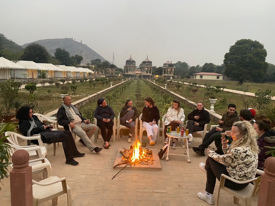 Groupe de personnes assises autour d'un foyer avec des tentes en arrière-plan.