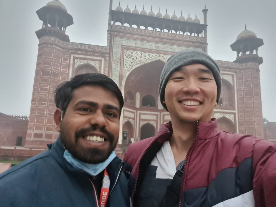 Two people taking a selfie in front of a red sandstone building.