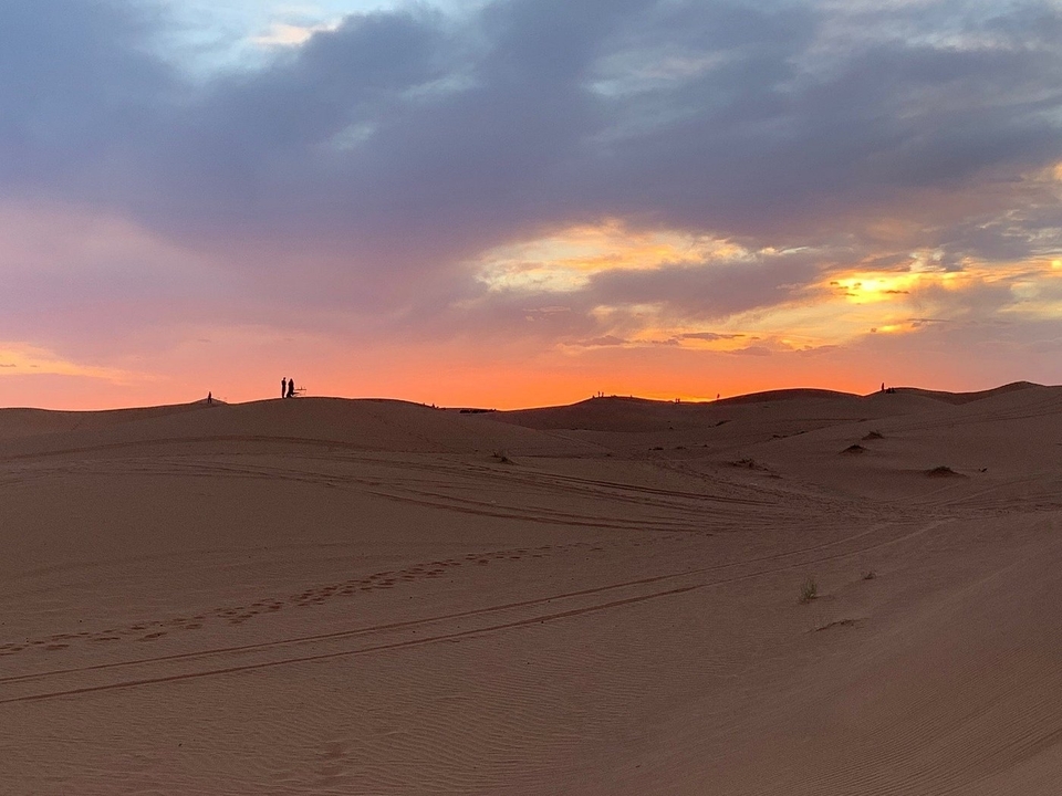 Zandduinen bij zonsondergang met een kleurrijke hemel.