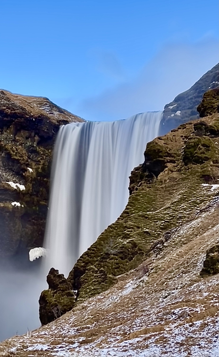 Waterfall cascading down a cliff with snow patches around.