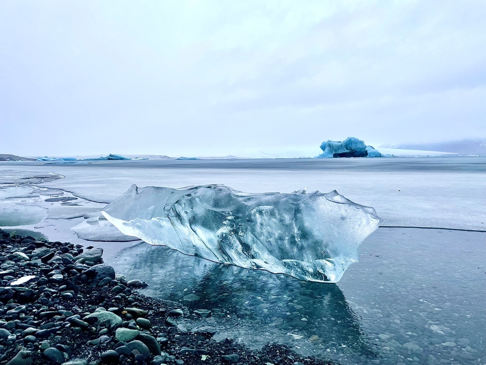 Crystal clear ice chunk on a beach with ocean in the background.