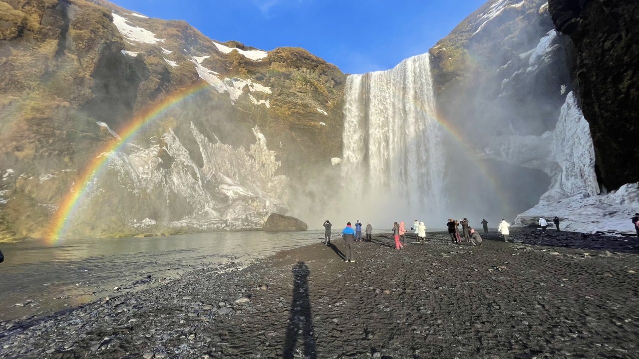 Tourists standing in front of a large waterfall with a rainbow.