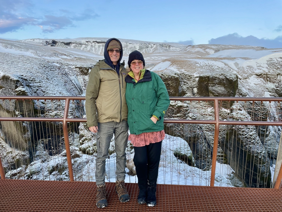 Couple posing on a viewing platform overlooking a snowy canyon.