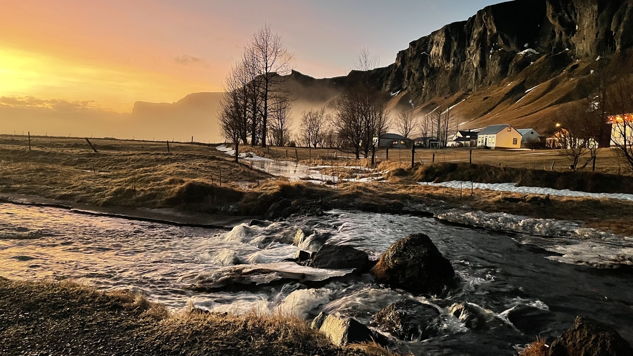 Beautiful landscape with a stream, houses, and a colorful sky at sunset.