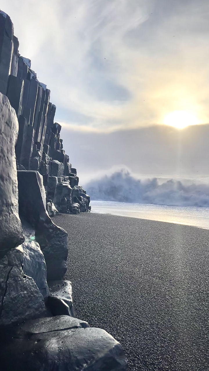 Waves hitting the black basalt columns on a beach.