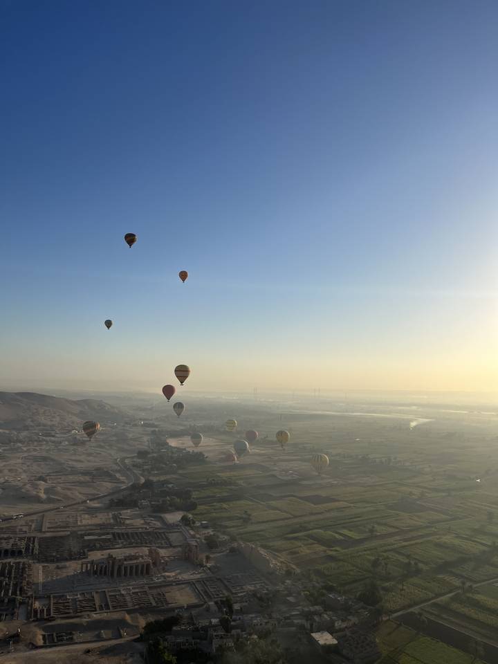 Hot air balloons over fields at sunrise.