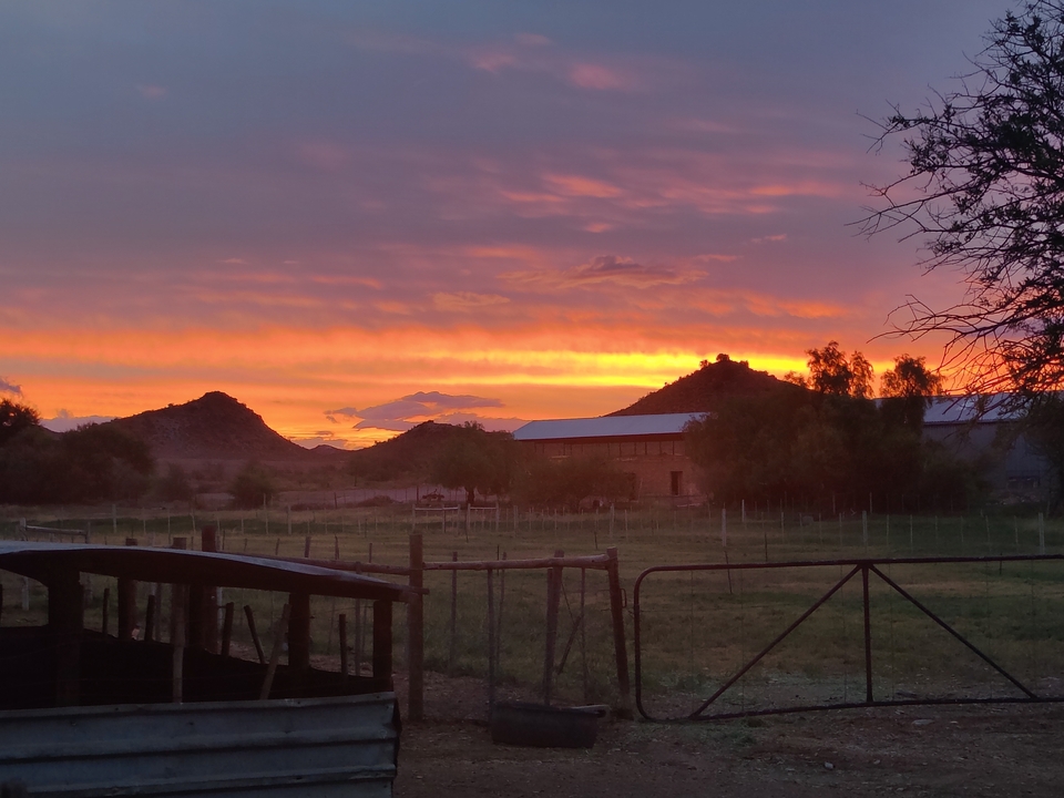 Sunset over rural landscape with fences and hills.