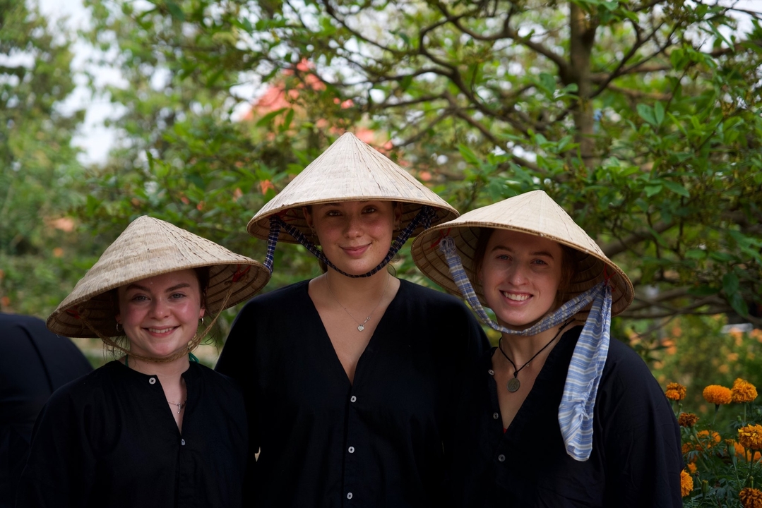 Three people wearing conical hats smiling outdoors.