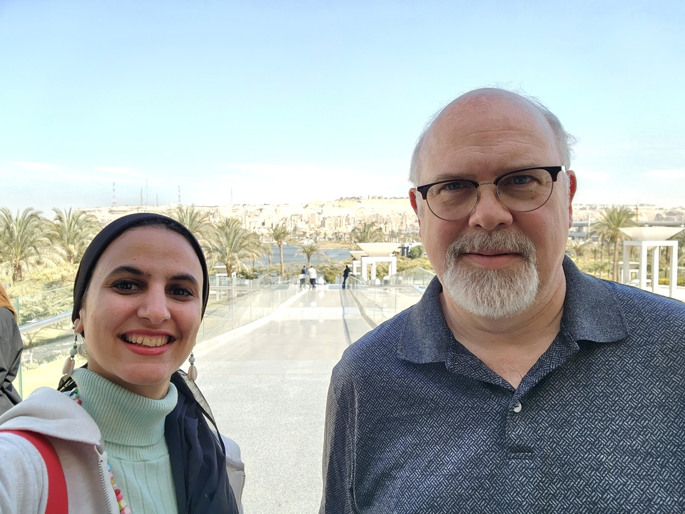 Deux personnes debout dans une zone touristique ensoleillée en plein air.