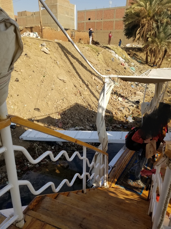 People walking along a riverbank with a sandy path.
