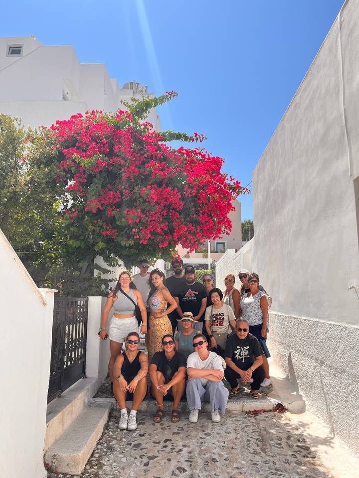 A group of people sitting and standing around a vibrant bougainvillea bush.