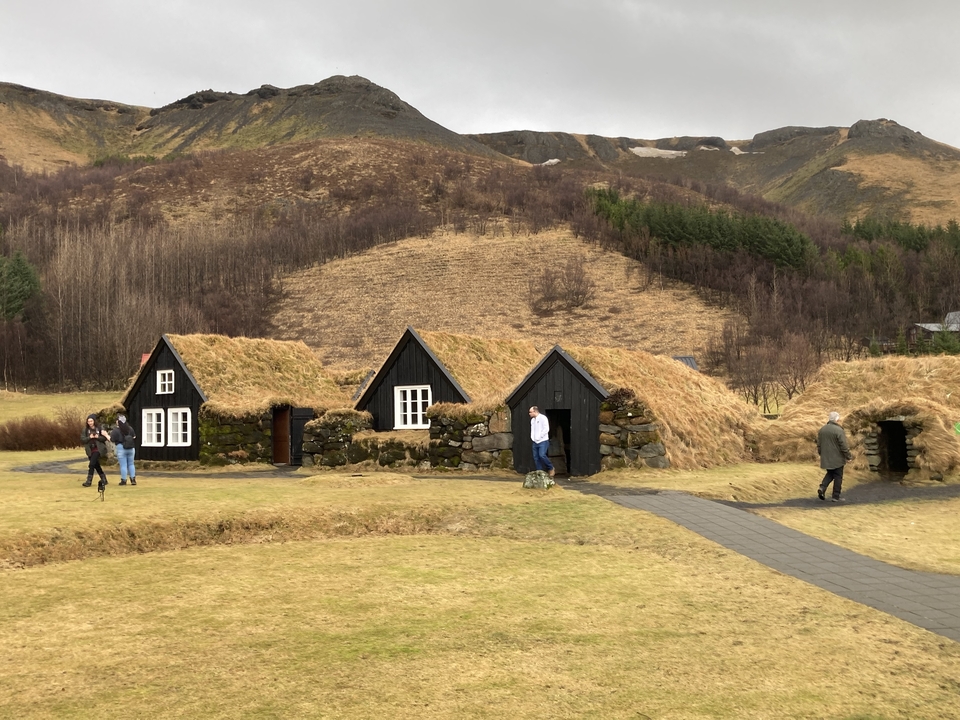 Grass-roofed houses on a green landscape with hills in the distance.