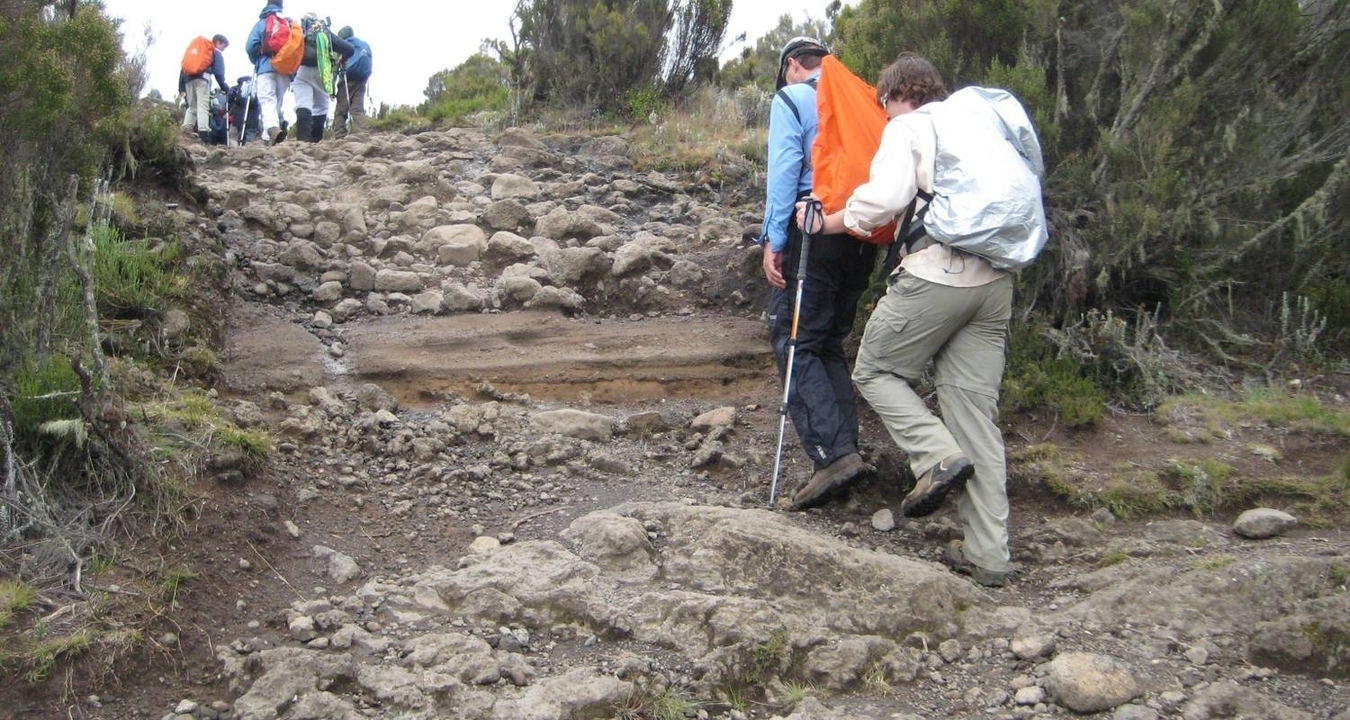 Groupe de randonneurs sur un sentier rocheux dans un paysage accidenté.