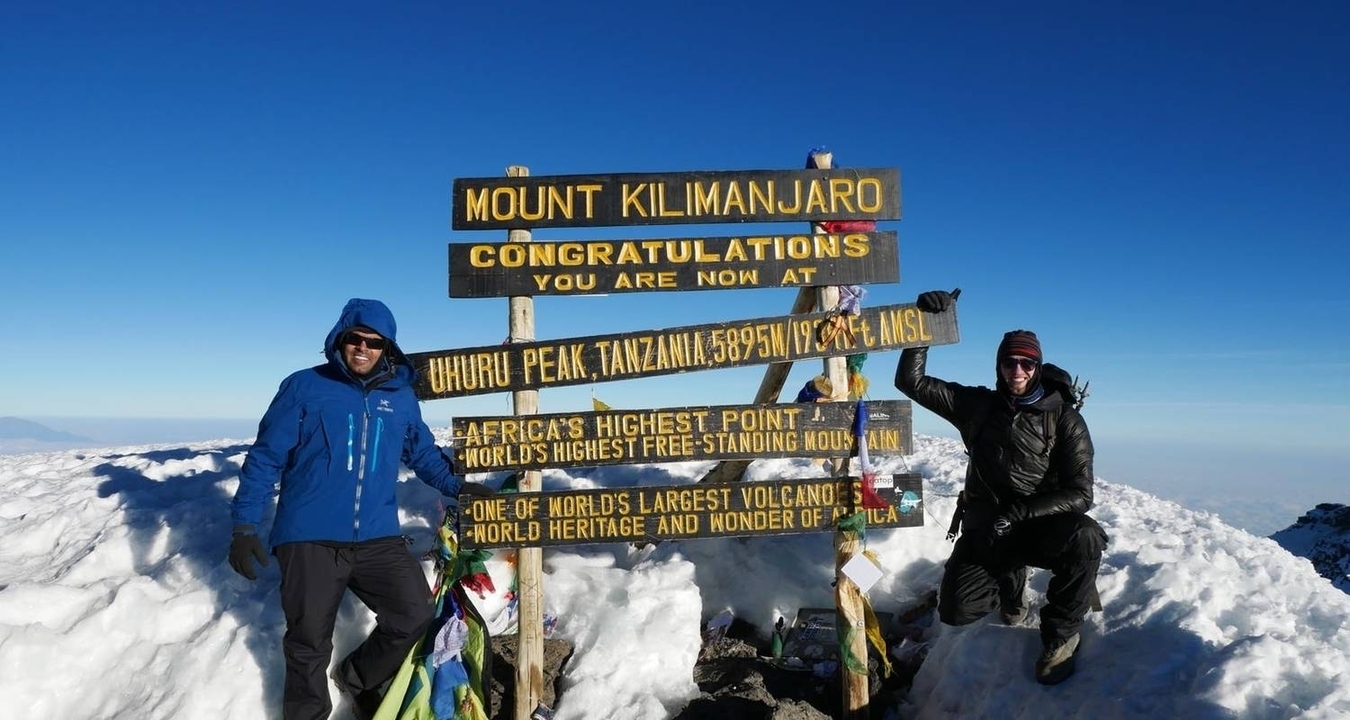 Deux personnes posant devant le panneau du sommet du mont Kilimandjaro.