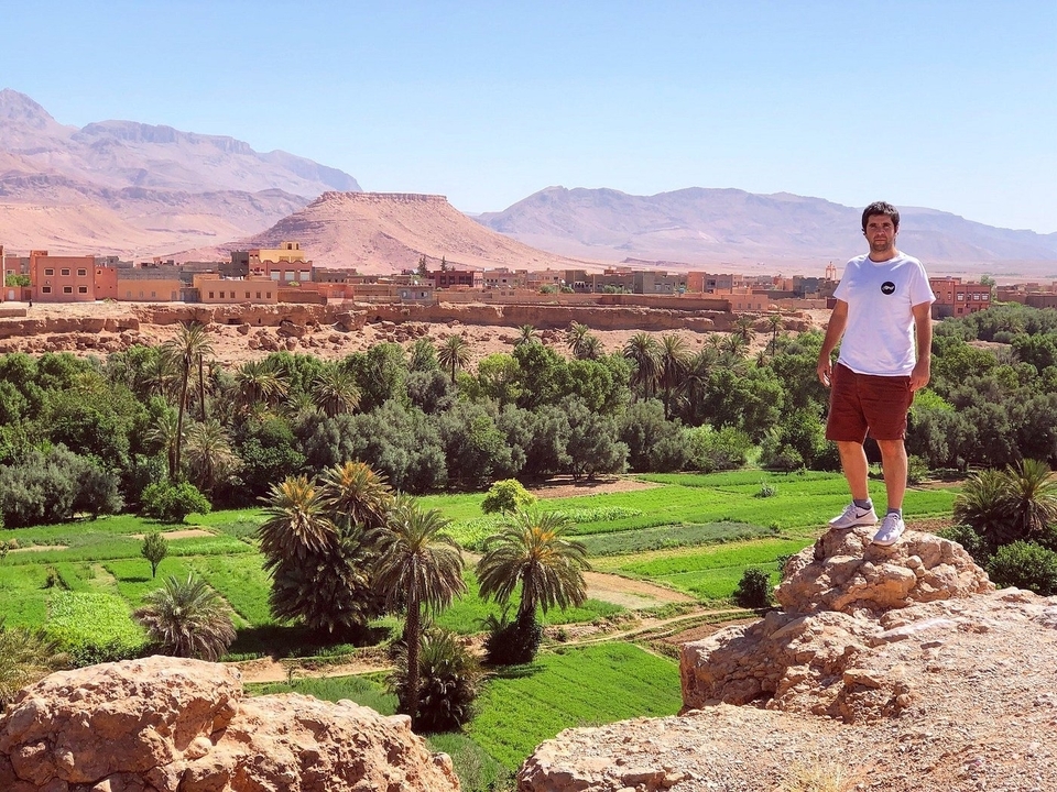 A man standing on a rock with a vibrant town and mountains in the background.