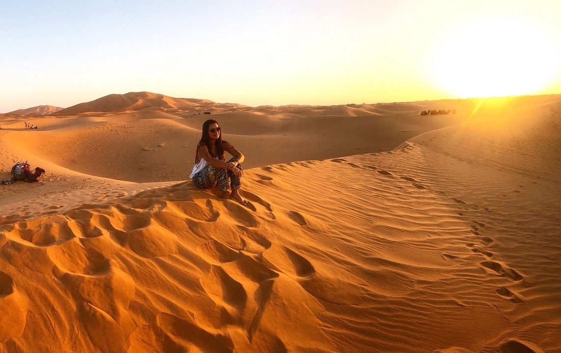 A person sitting on sand dunes during sunset.