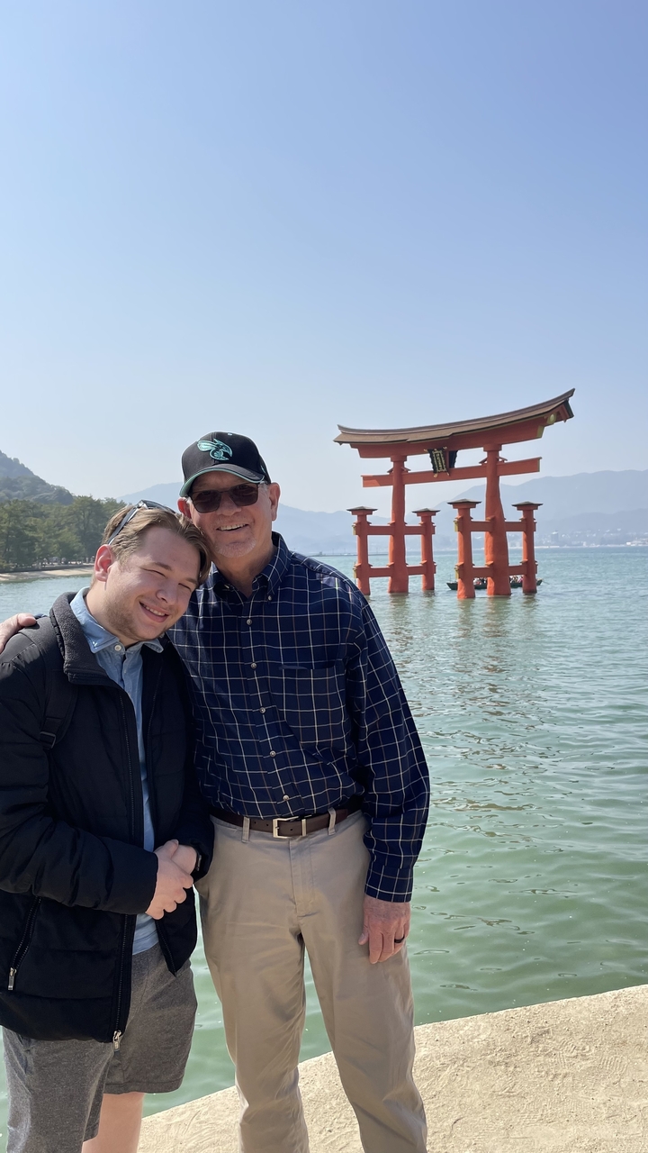 Two people posing with Itsukushima Shrine floating Torii in the background.