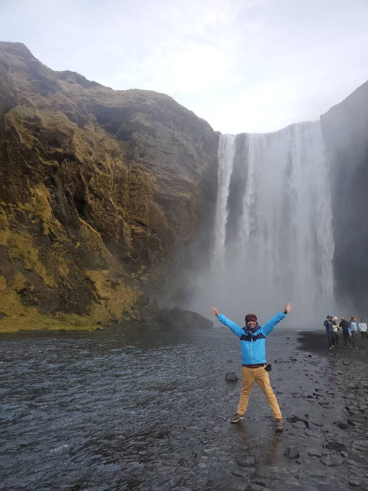 Person posing in front of a massive waterfall.