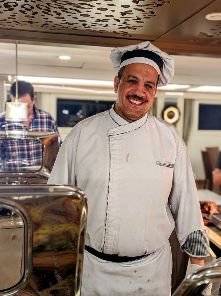 Chef smiling in a dining area on a cruise.