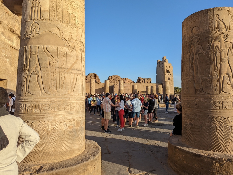 Tourists exploring a historical site with decorated pillars.