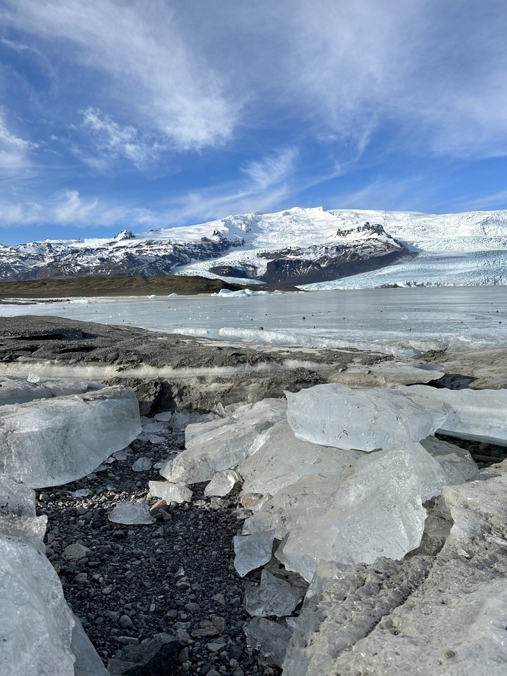 Frozen lake with ice chunks surrounded by snowy mountains.