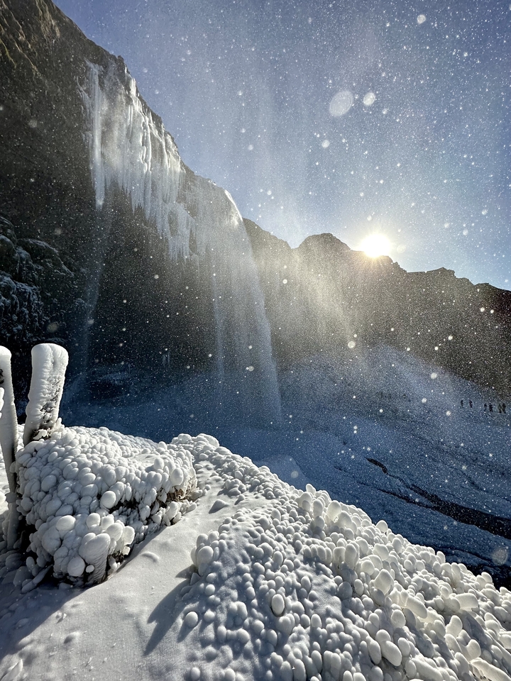 Waterfall with sunlight creating mist and ice formations.