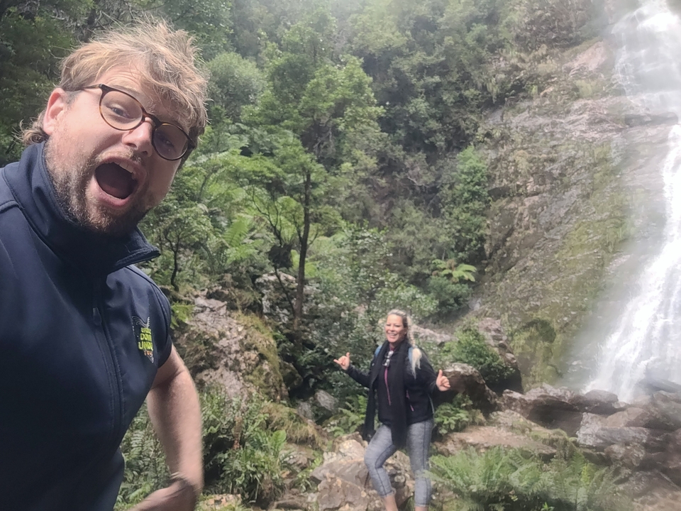 Two people posing with a waterfall in the background.