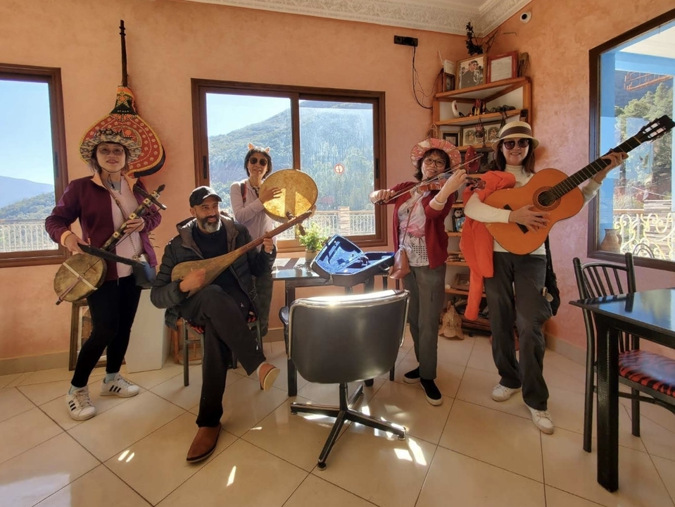 Group of people posing with musical instruments in a room with a view outside.