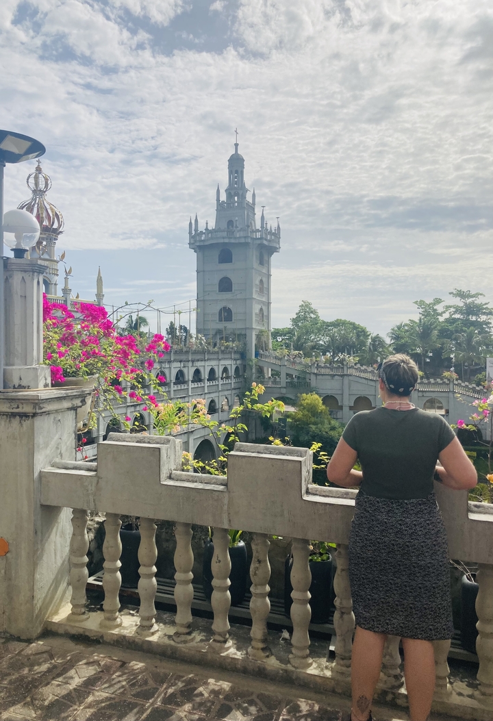 A woman looking at a large religious stone structure, lush garden in the foreground.