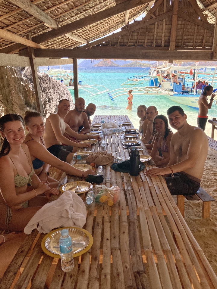 Group of people dining at a wooden table by a beach.