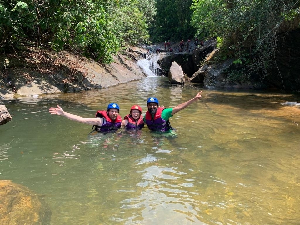 Three people posing in a river in front of a waterfall.