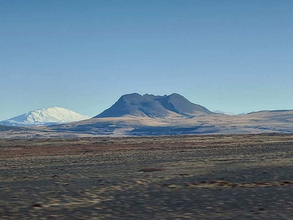 Distant view of ice-capped mountain peaks over a barren landscape.
