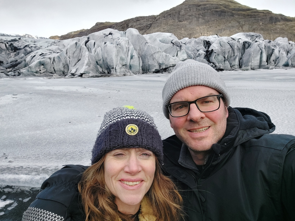 Couple posing in front of a glacier with icy formations.