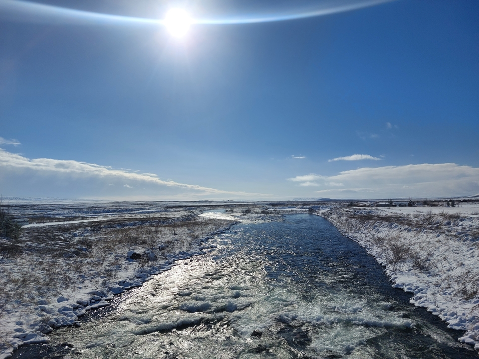 Snowy landscape with a clear river under a bright sun.