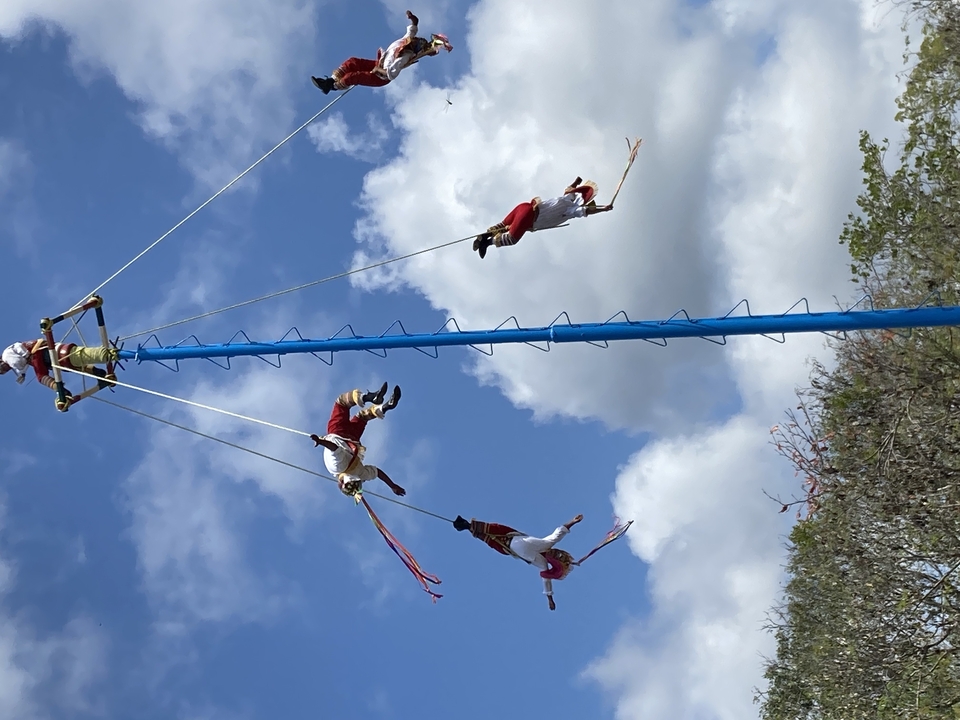 Performers in traditional costumes suspended on a pole in an aerial dance.