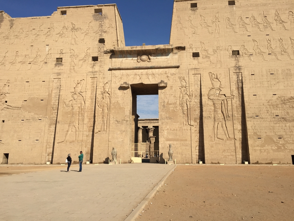 Grande porte en pierre de l'Égypte antique avec sculptures et touristes.