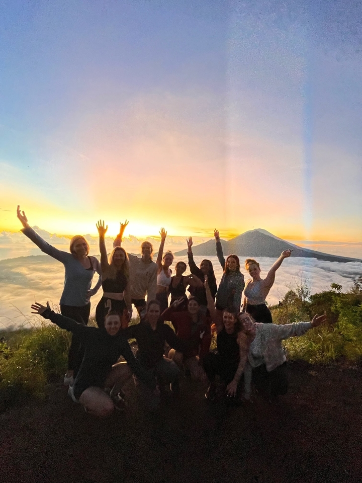 Group of people celebrating a sunrise or sunset on a mountain with a sea of clouds.