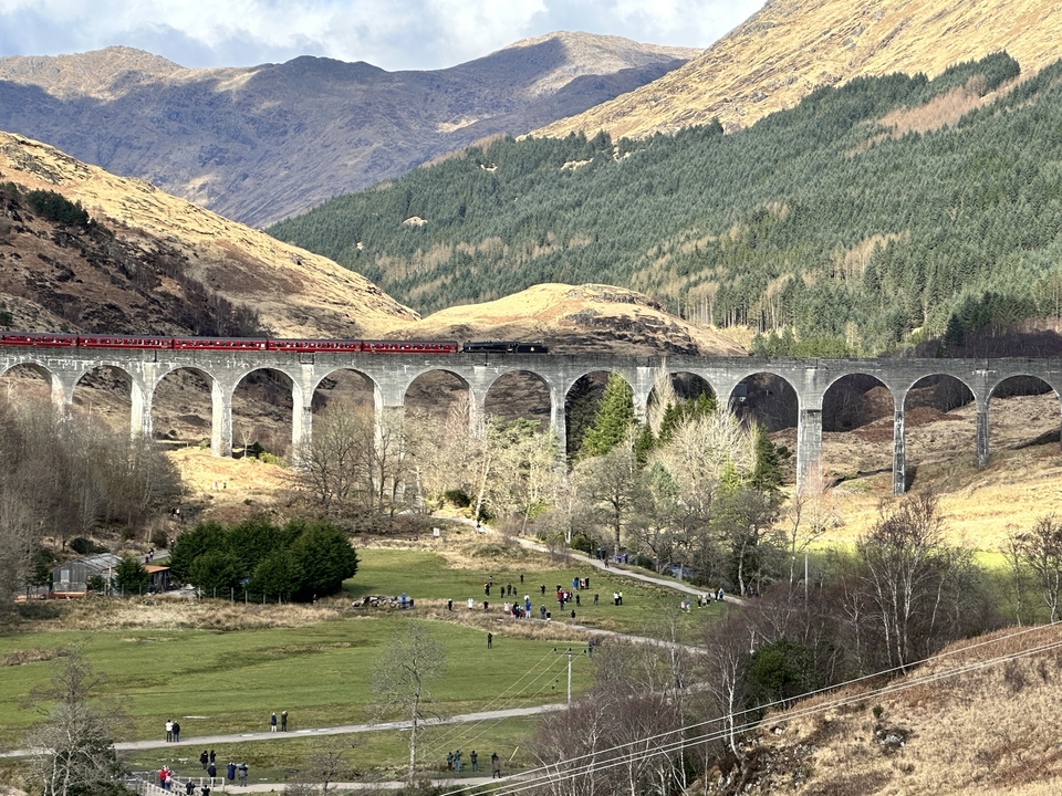 A train crossing a historic viaduct with mountains in the background.