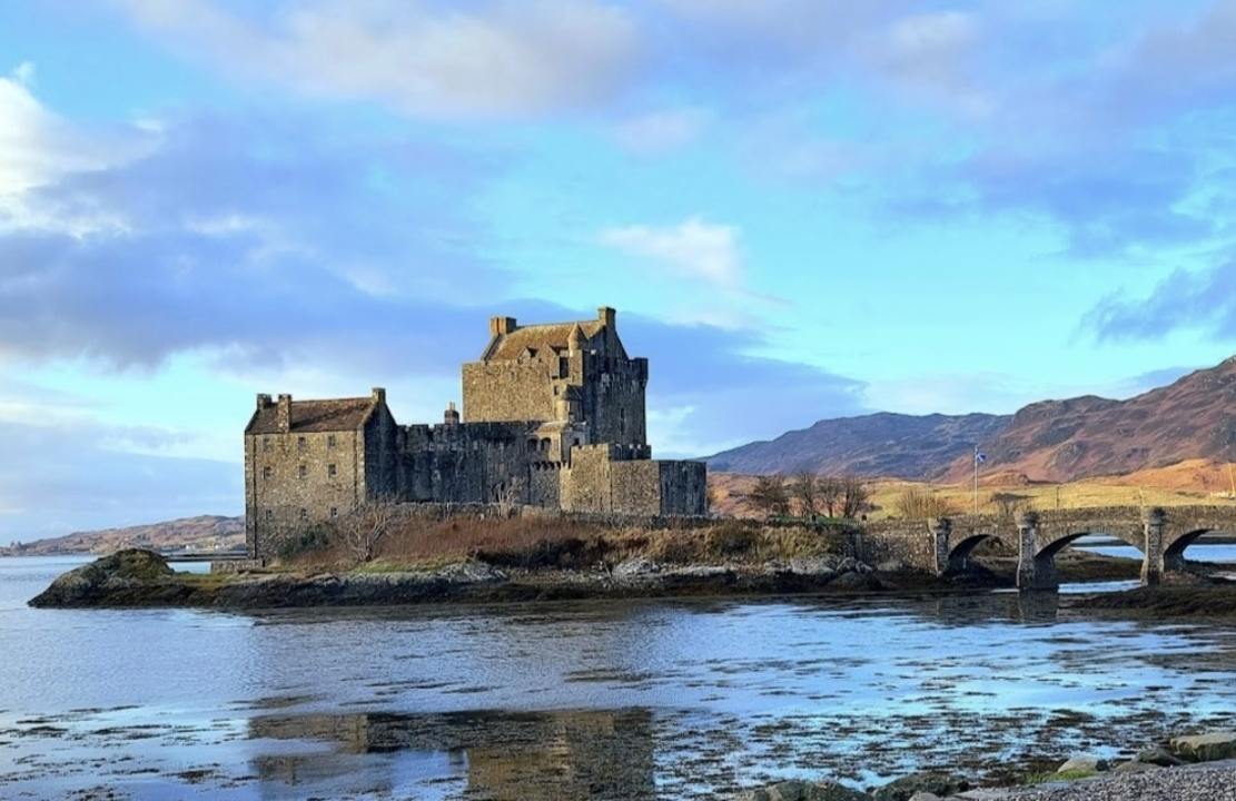 Eilean Donan Castle surrounded by water and hills.