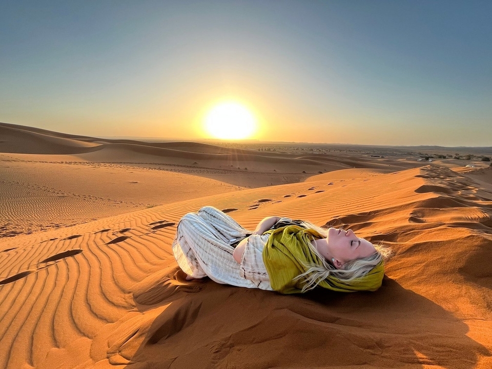 Person lying on sand dunes with sunset in the background.