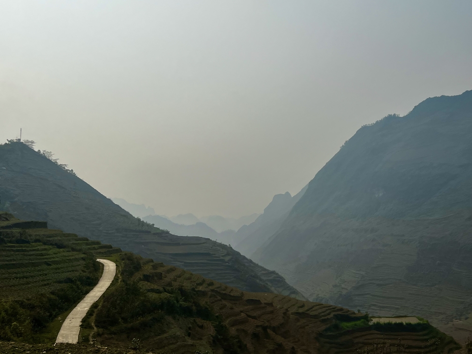 Terraced fields leading towards mountains with a hazy sky.